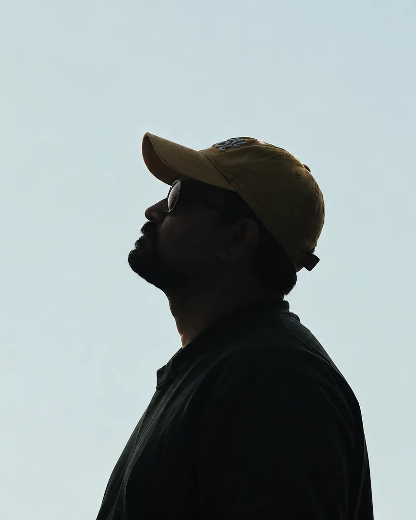 Atul Arvind in profile against a pale sky, wearing a cap and sunglasses